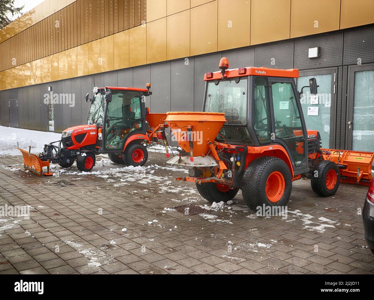 Salt spreader and snow plough parked outside an industrial structure in a winter day with snow Stock Photo
