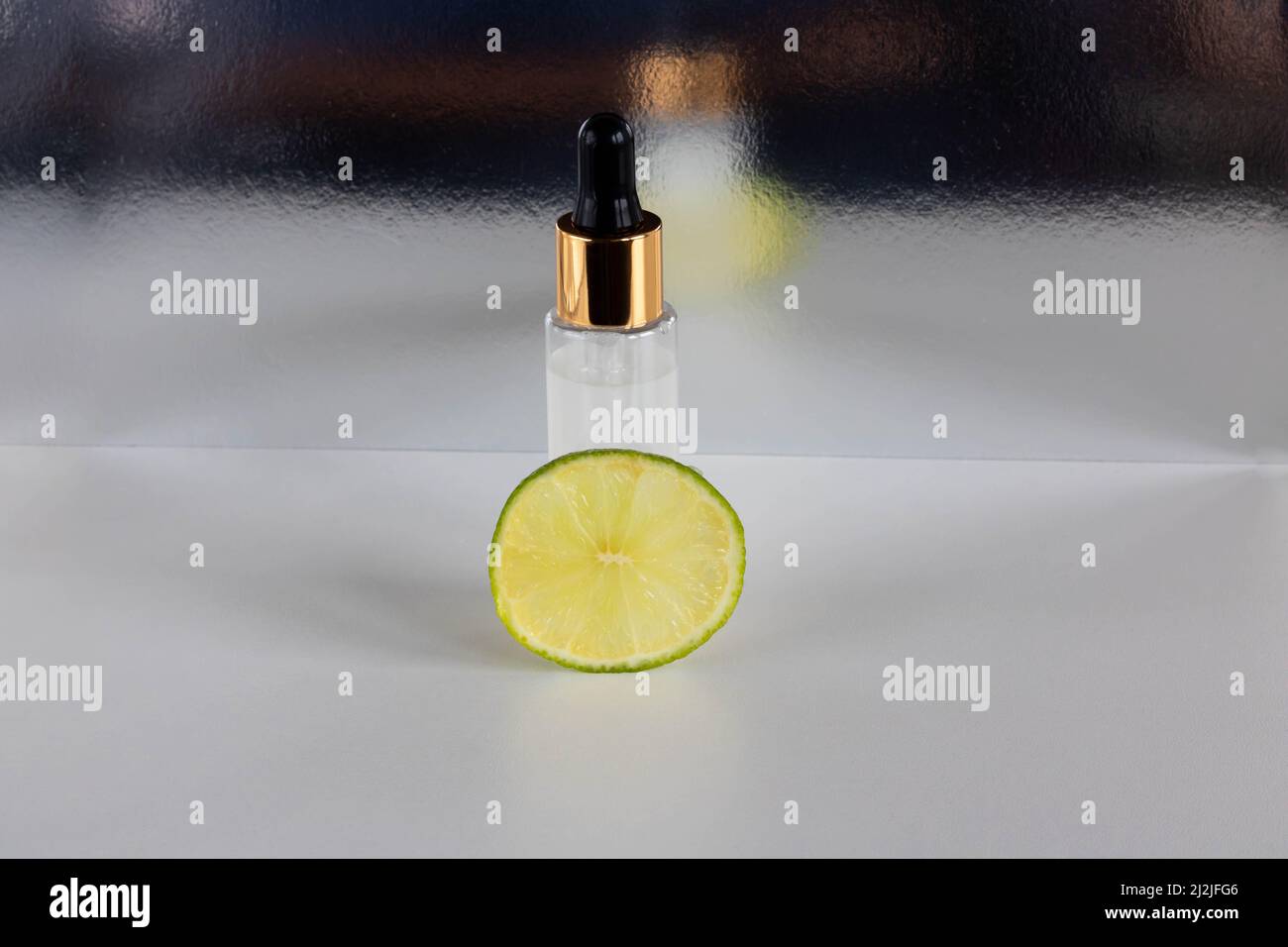 A piece of lime and a frosted bottle with an eyedropper, highlighted on a glossy background. The layout is suitable for cosmetics design Stock Photo
