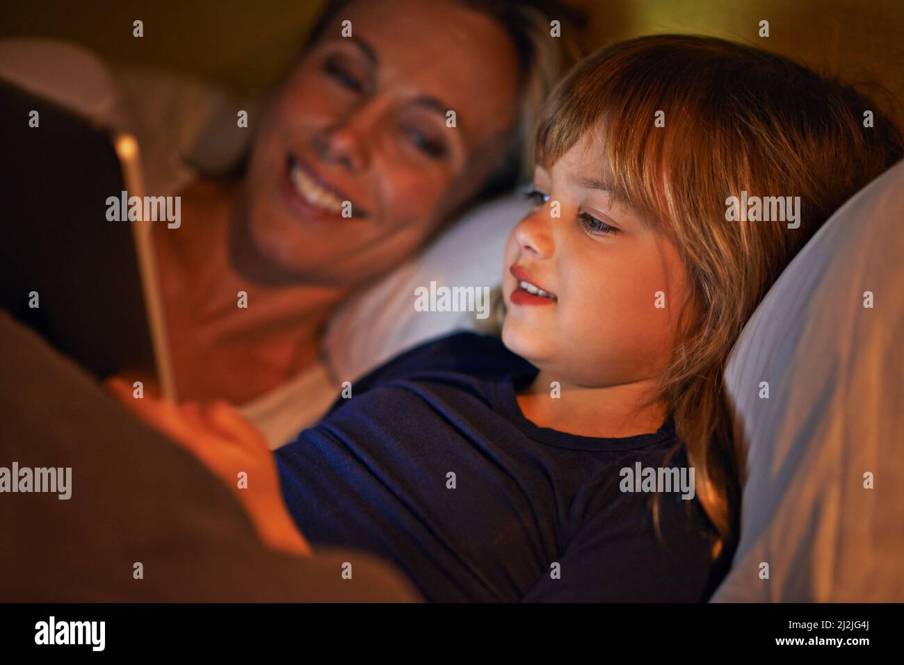 Enjoying time together before bed. A mother and daughter lying in bed with a digital tablet. Stock Photo