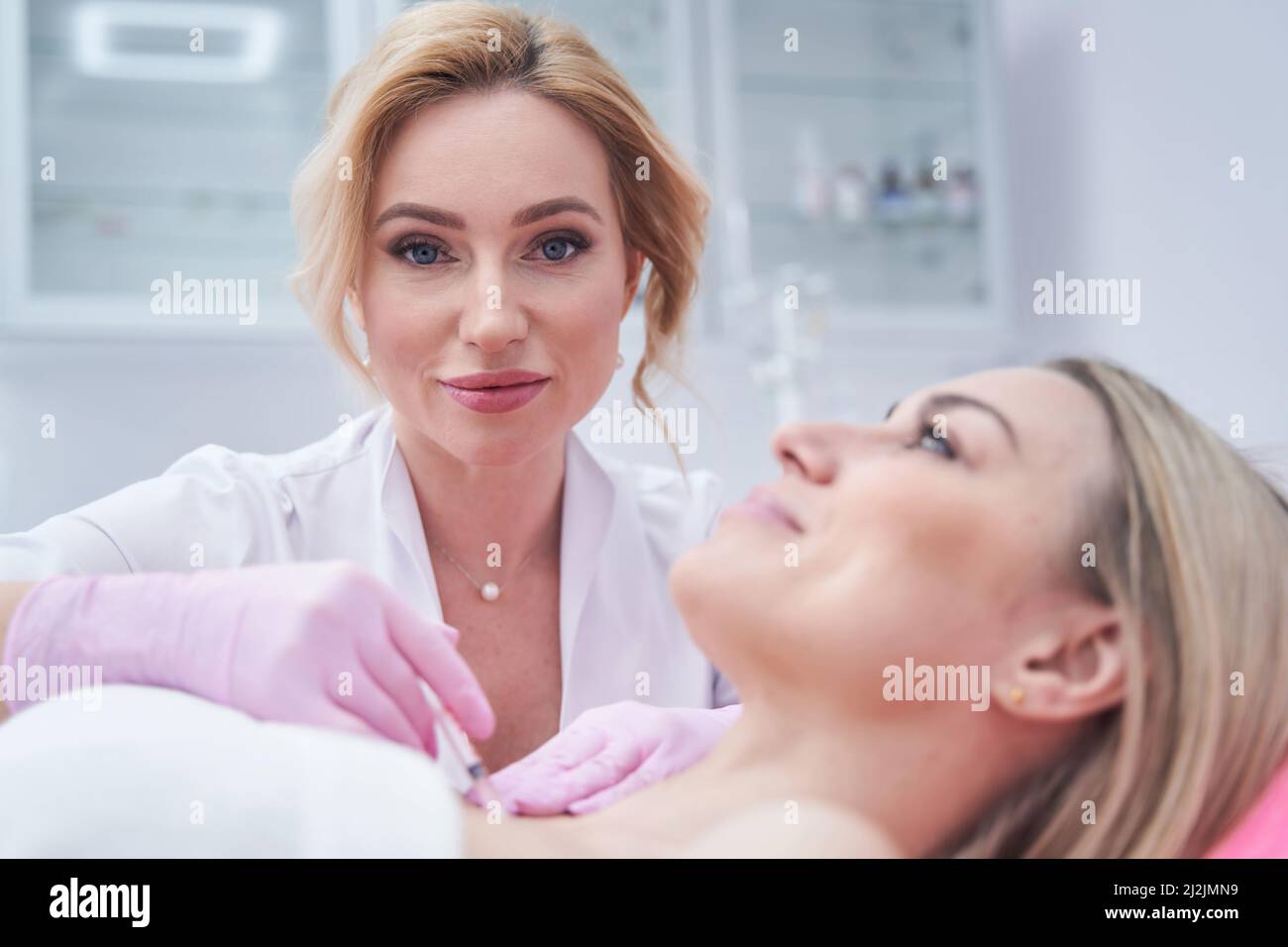 Experienced dermatologist injecting dermal filler into decolletage area of patient Stock Photo