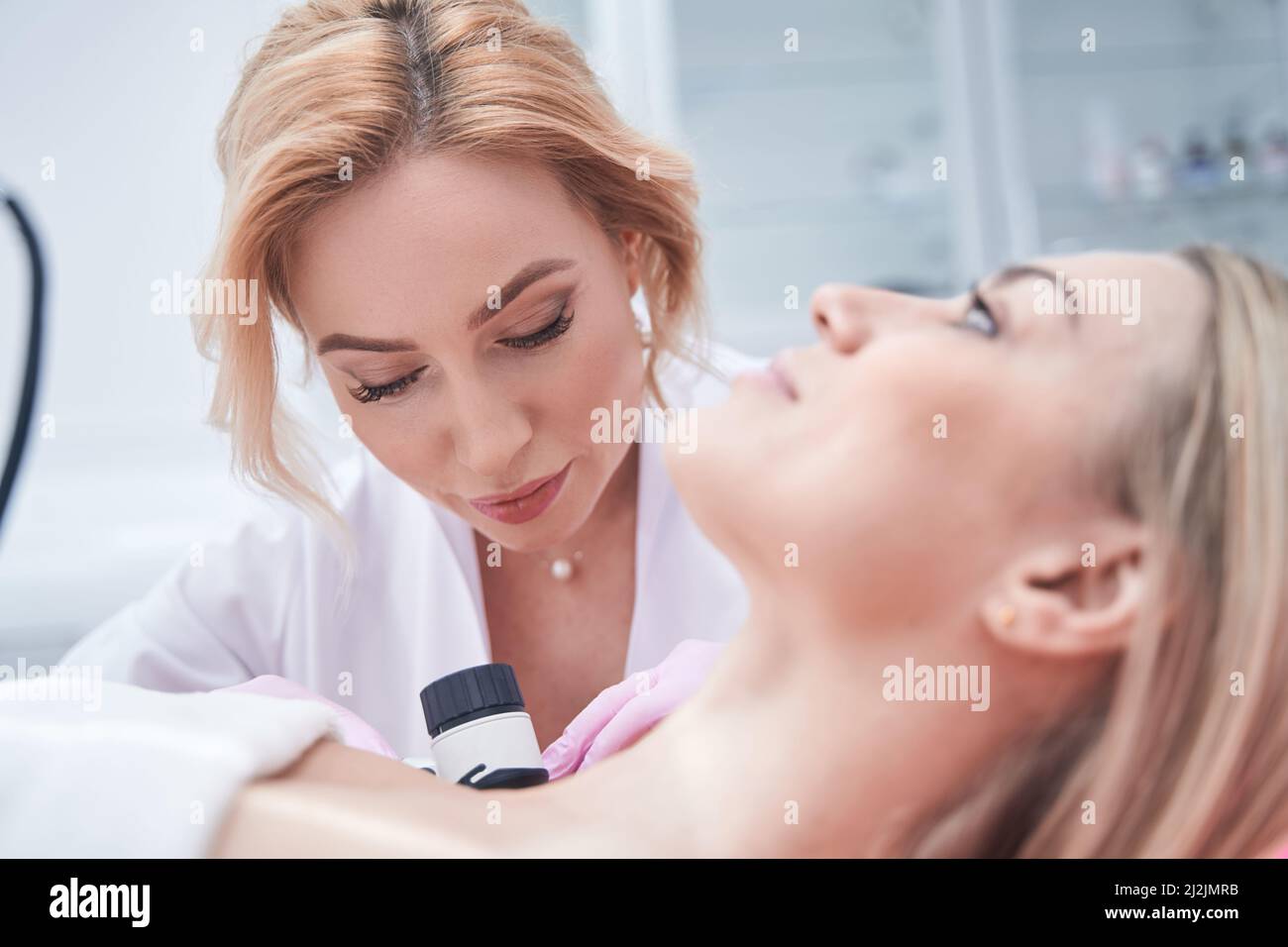 Concentrated qualified middle-aged dermatologist performing dermatoscopy procedure Stock Photo