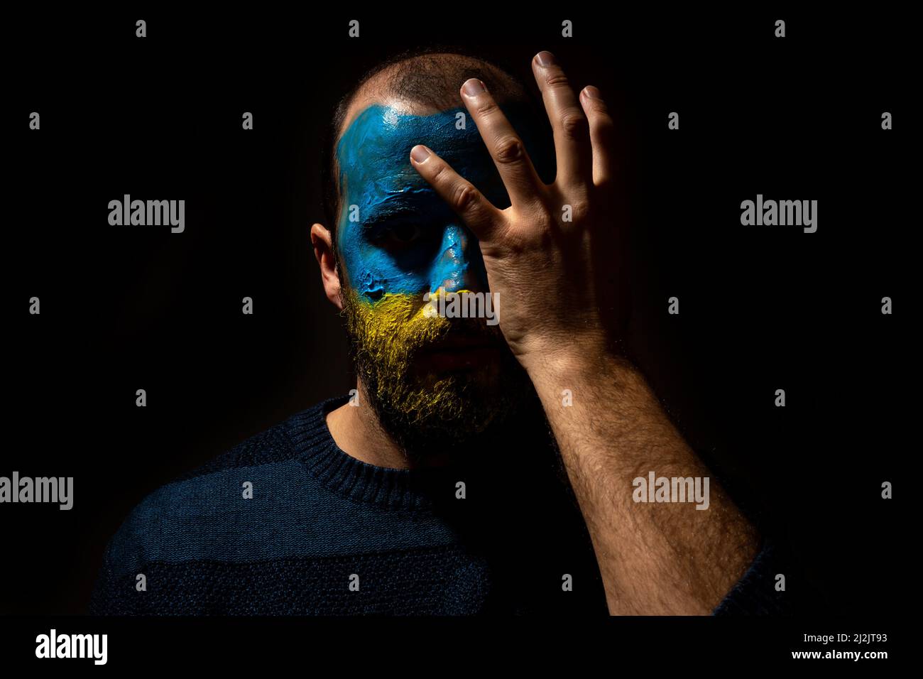 The Concept Stop war, the conflict between Ukraine and Russia. Portrait of a young man with his face painted in the blue and yellow colors of the flag Stock Photo