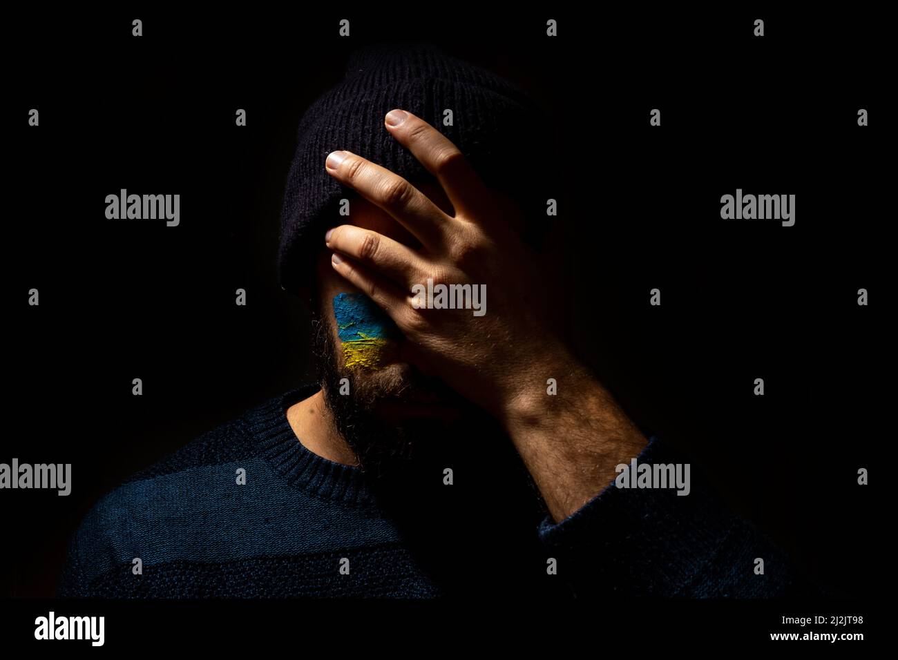 The Concept Stop war, the conflict between Ukraine and Russia. Portrait of a young man with his face painted in the blue and yellow colors of the flag Stock Photo