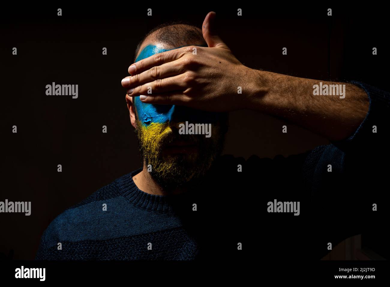 The Concept Stop war, the conflict between Ukraine and Russia. Portrait of a young man with his face painted in the blue and yellow colors of the flag Stock Photo