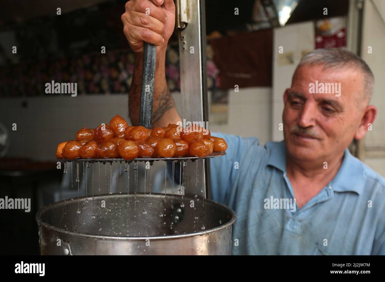 Nablus, Ramadan at a local market in the West Bank city of Nablus. 2nd Apr, 2022. A vendor makes Luqmat al-Qadi sweets, a traditional pastry made of leavened and deep fried dough, on the first day of the holy month of Ramadan at a local market in the West Bank city of Nablus, April 2, 2022. Credit: Nidal Eshtayeh/Xinhua/Alamy Live News Stock Photo