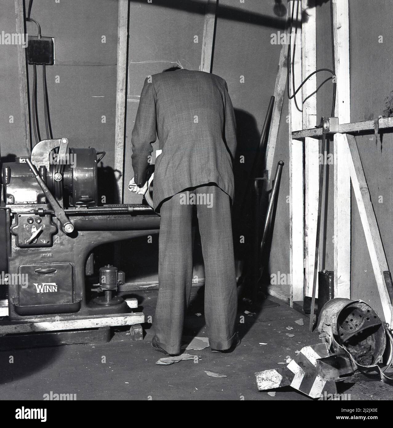 1950s, historical, in a internal construction site, a man in a suit using a bench type machine tool, made by Winn, possibly for wood working, Port Talbot, Wales, UK. Stock Photo