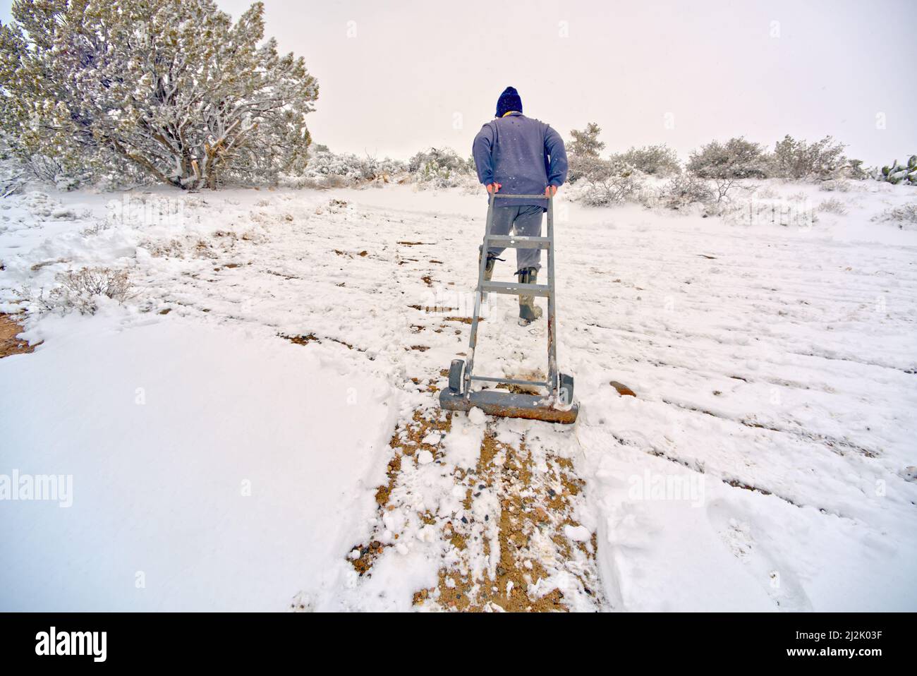 Rear view of a man using an upside down appliance Dolly to clear snow, Chino Valley, Arizona, USA Stock Photo