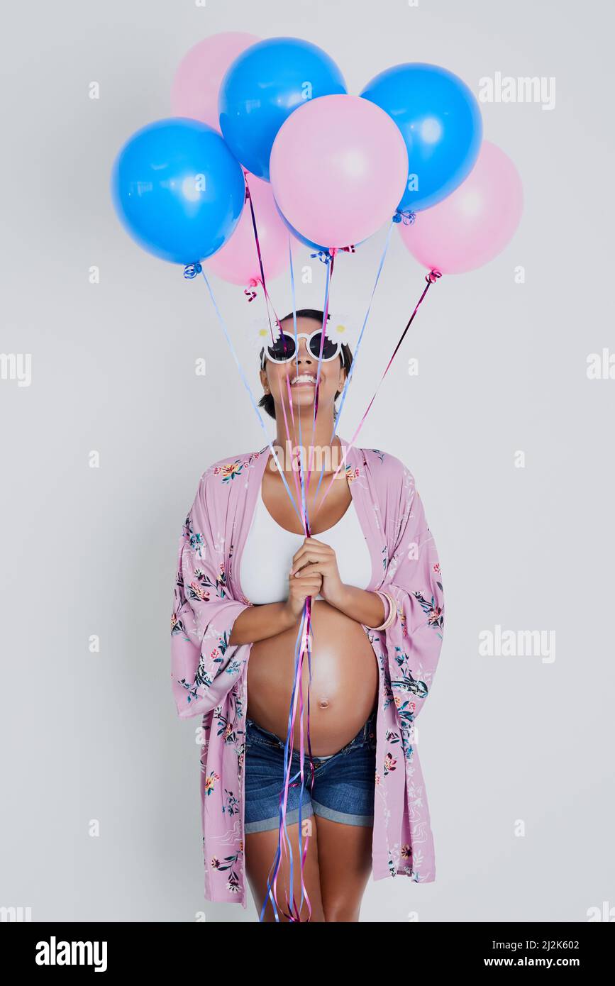 Girl,boy pink or blue what will my baby be. Studio shot of a beautiful young pregnant woman holding blue and pink balloons against a gray background. Stock Photo