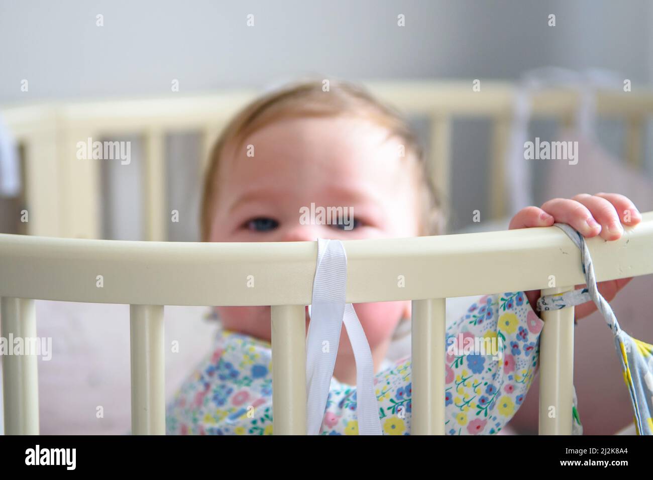 Cute girl of ten months old, playing alone in a crib at home in the