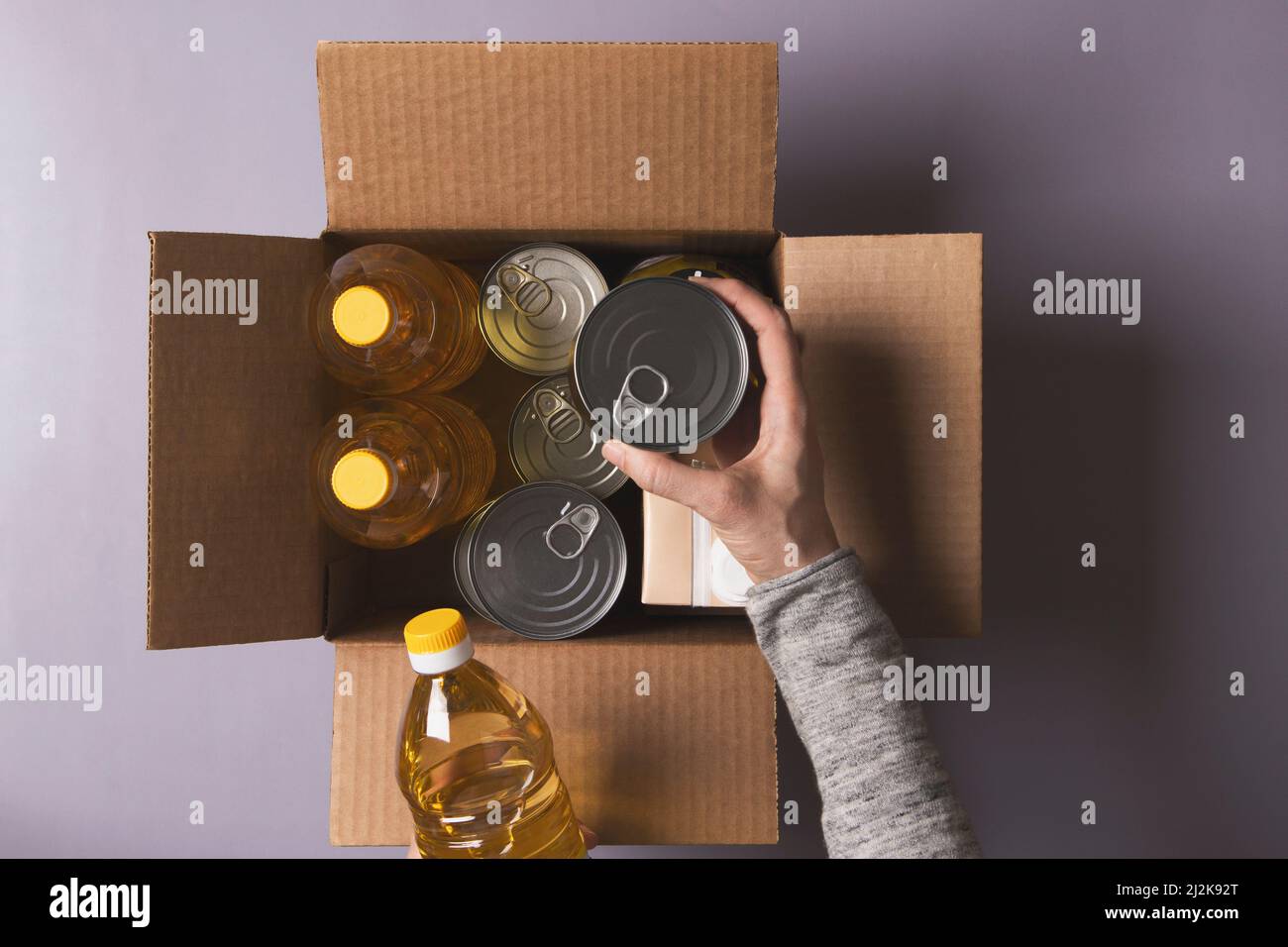 Volunteer hands collecting food into donation box. Top view to