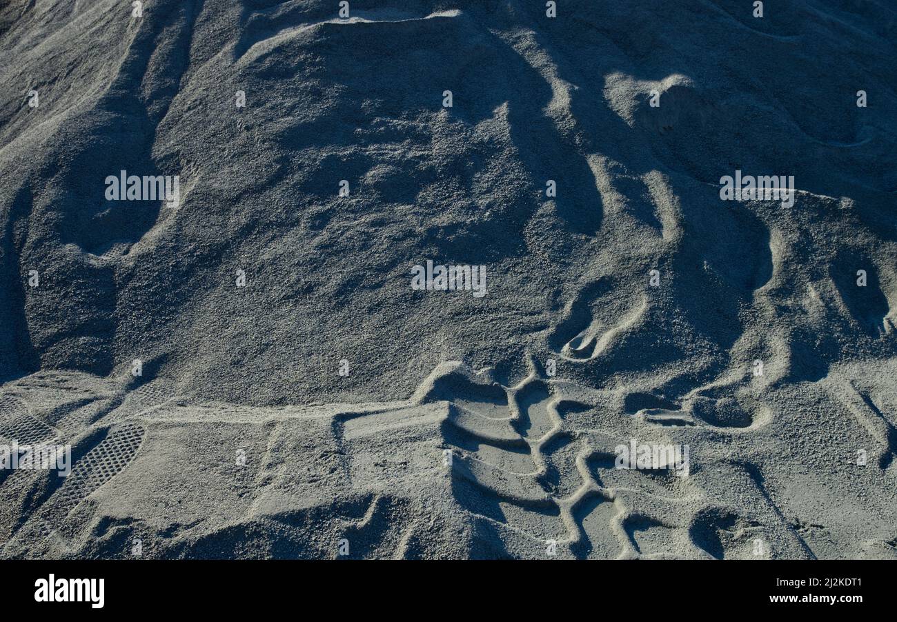 traces of upward shoe prints and skid marks in grey sand Stock Photo