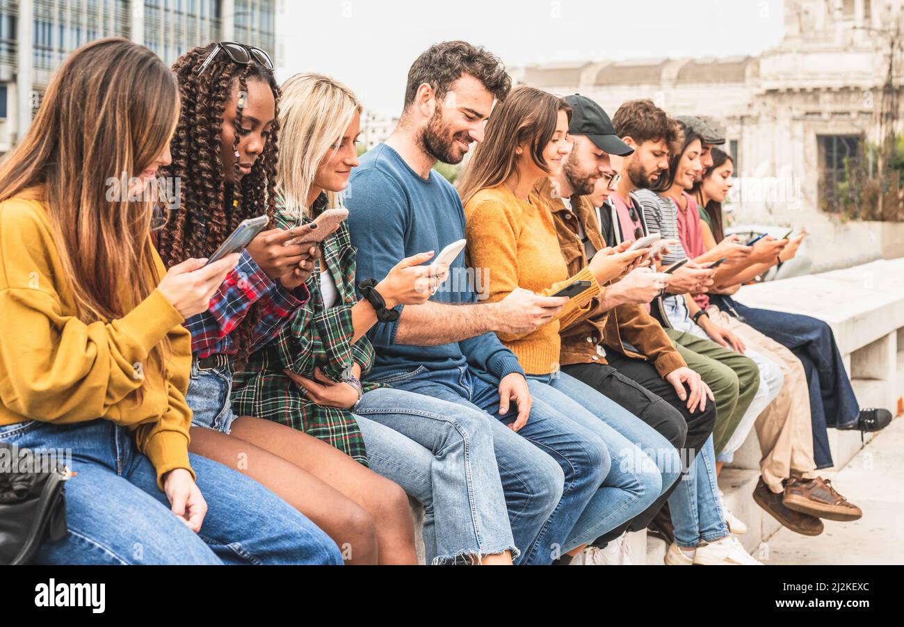 large group of people sitting outdoor and looking at smart phones, social network and media addicted young person concept Stock Photo