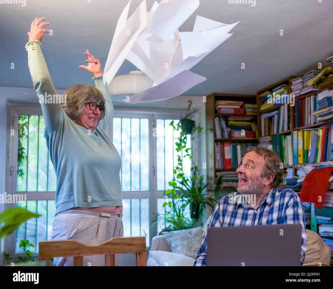 Senior couple quarrelling at home, financial problems in family, angry woman with man throwing sheets of paper in the air for a fit of anger Stock Photo