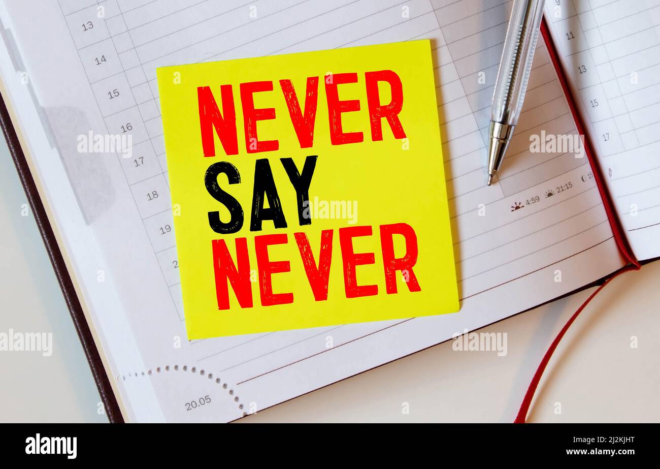 Closeup on businessman holding a card with text NEVER SAY NEVER, business concept image with soft focus background and vintage tone Stock Photo