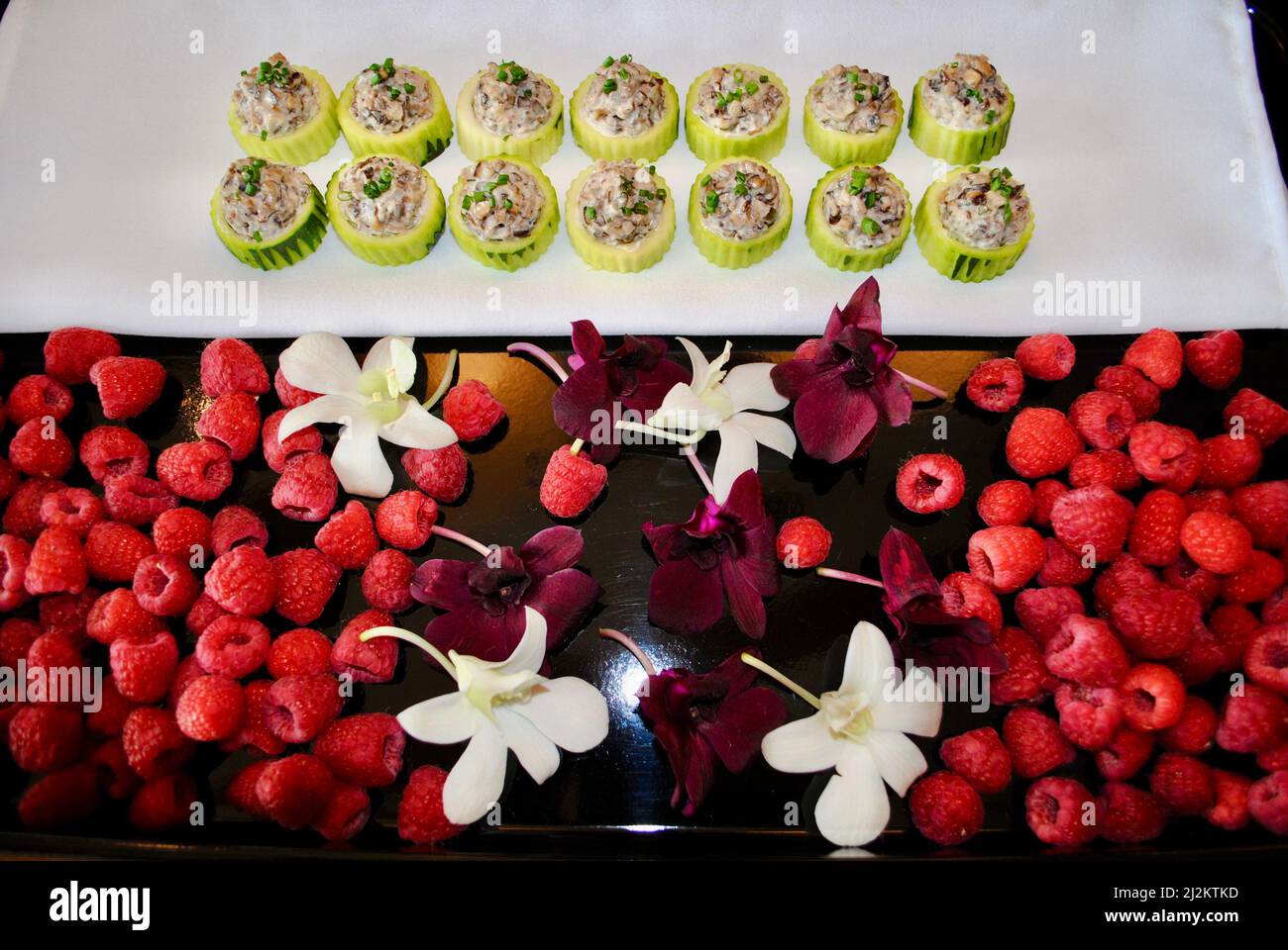Cucumber cups filled with wild mushroom salad on tray decorated with raspberries and orchids Stock Photo
