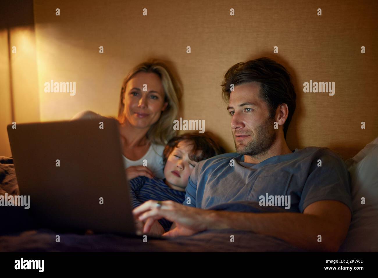 Drifting off to dreamland while watching movies. A young family lying in bed and looking at a laptop screen. Stock Photo