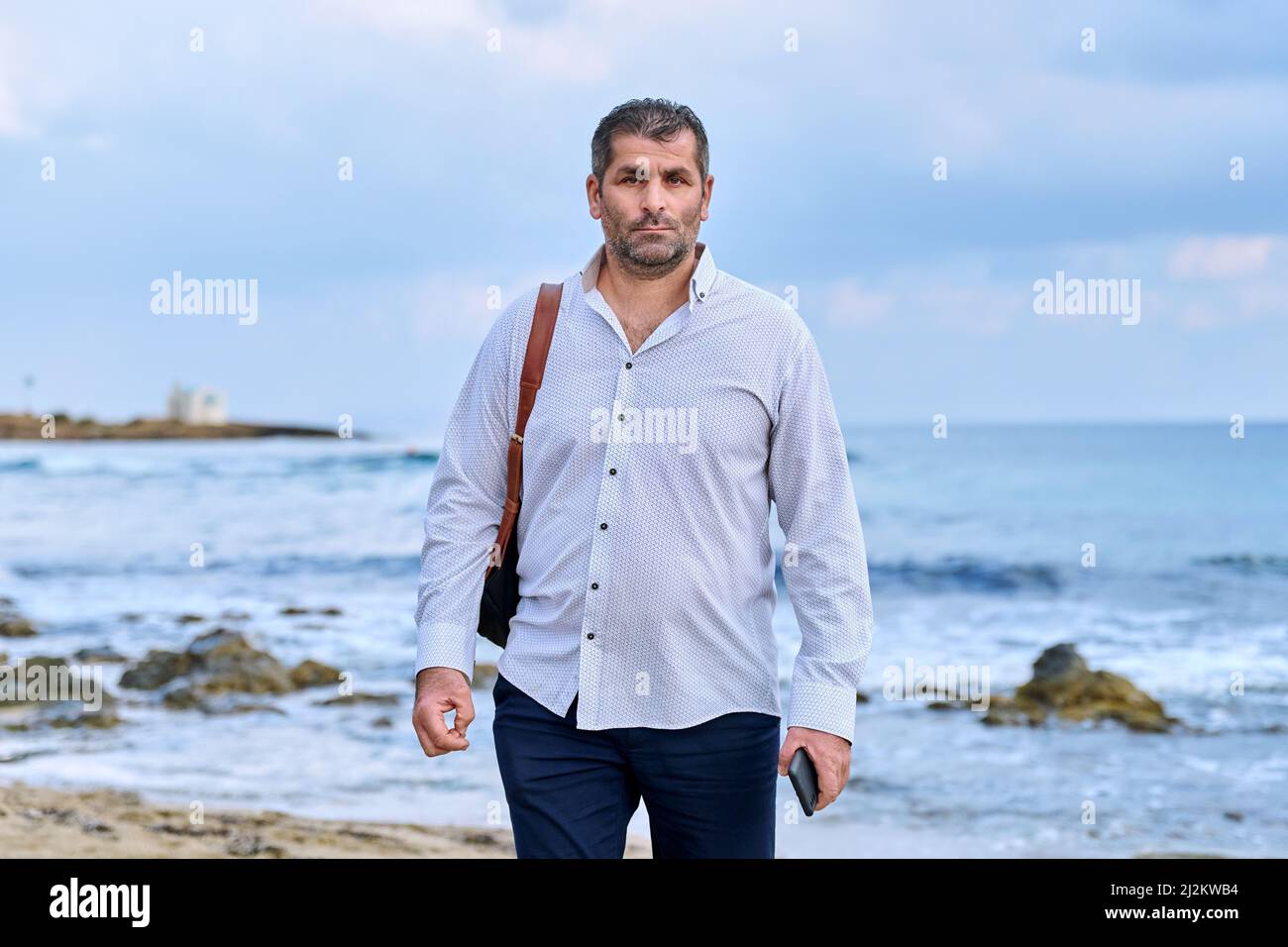 Serious confident successful mature man walking along the beach. Stock Photo