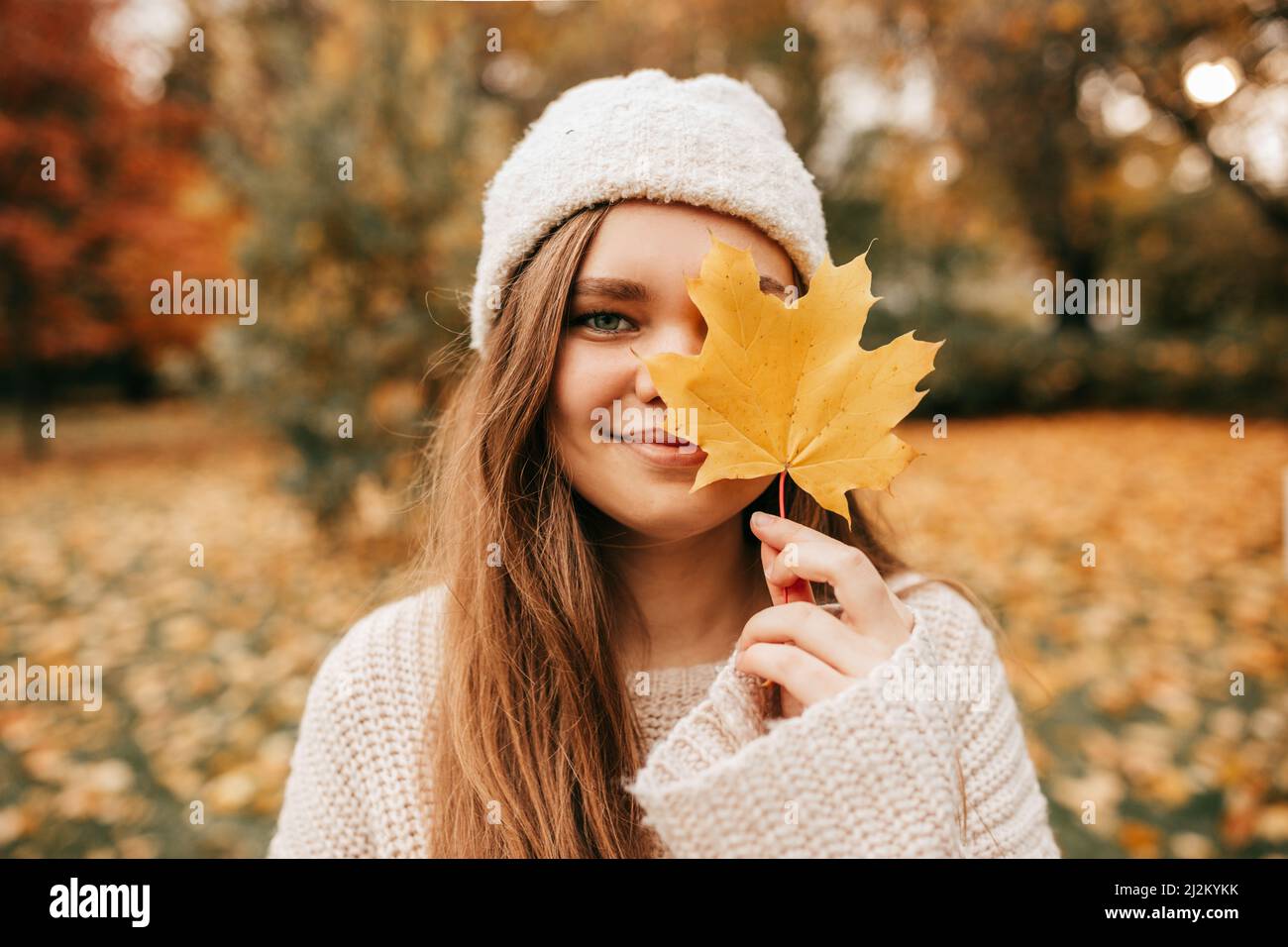 Portrait of close up face attractive blond smiling woman in hat, hold golden maple leaf face, close eye. Autumn Stock Photo
