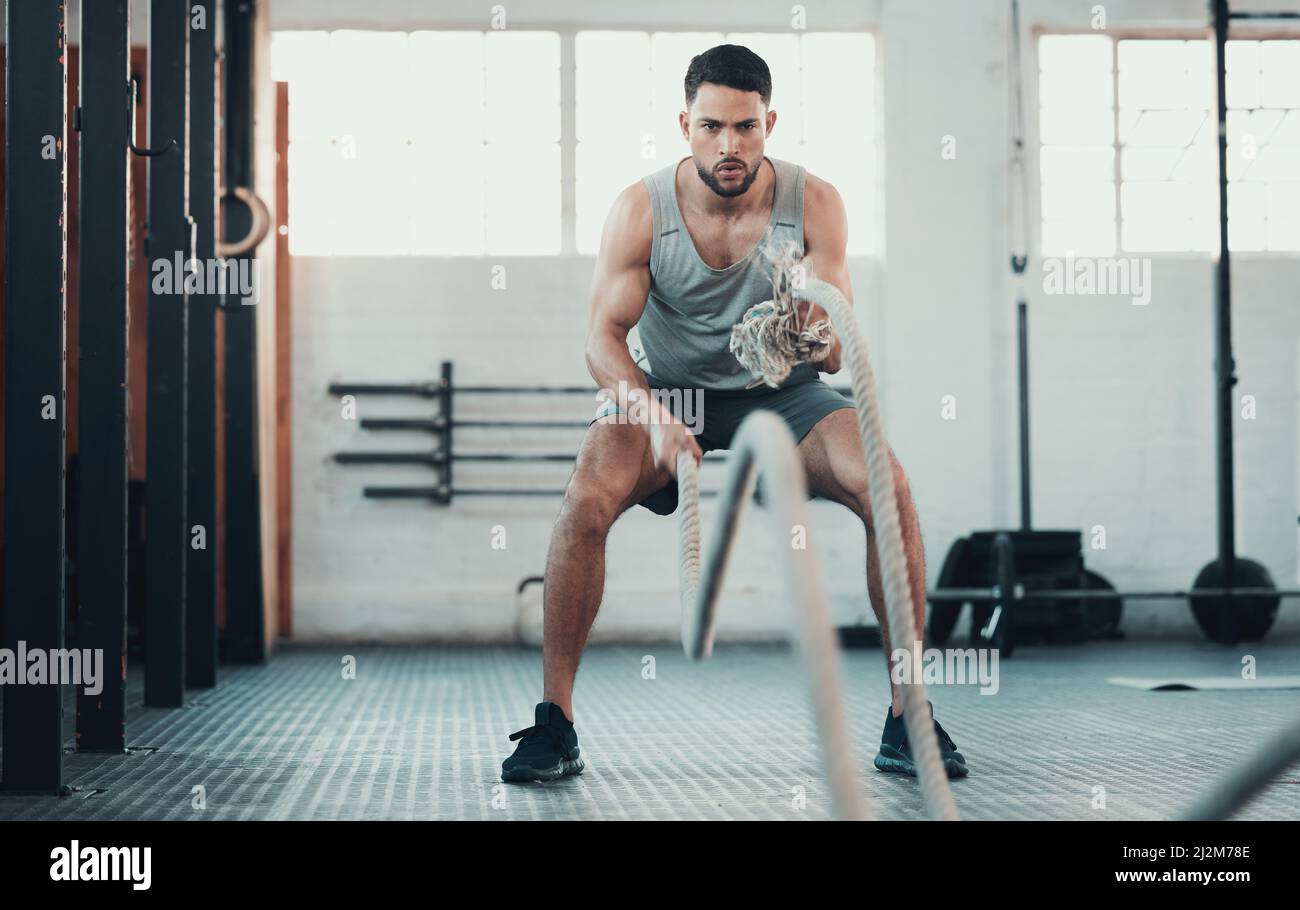 Im feeling the burn. Shot of a young man using the ropes in the gym to