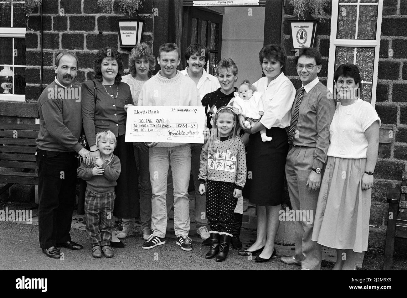 Huddersfield Town player Kieran O'Regan netted £264 for the Jolene Kaye Appeal when he collected a cheque from kind-hearted regulars of the Wooldale Arms. They raised the cash from raffles and donations. He is pictured receiving the cheque from fund-raising committee organiser Tricia Cooper (third right) who is seen holding baby Jolene. 5th November 1989. Stock Photo