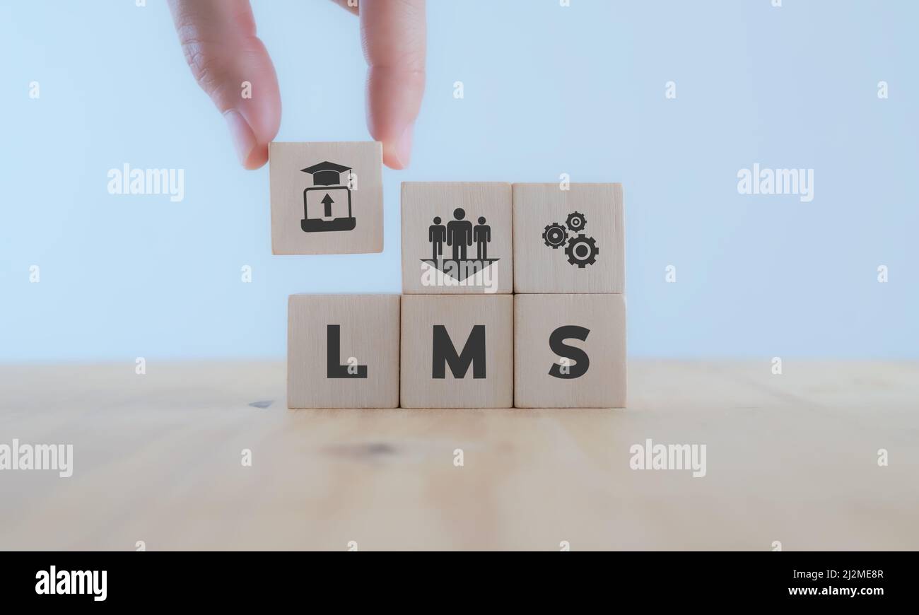 LMS Learning Management System concept.  Hand holds wooden cube with LMS symbols on beautiful light background with copy space. Online business educat Stock Photo