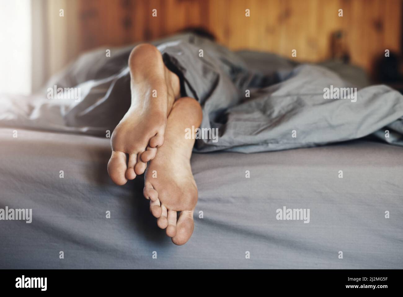 Toot tired to shower before bed. Closeup shot of a mans dirty feet while  hes sleeping in bed Stock Photo - Alamy