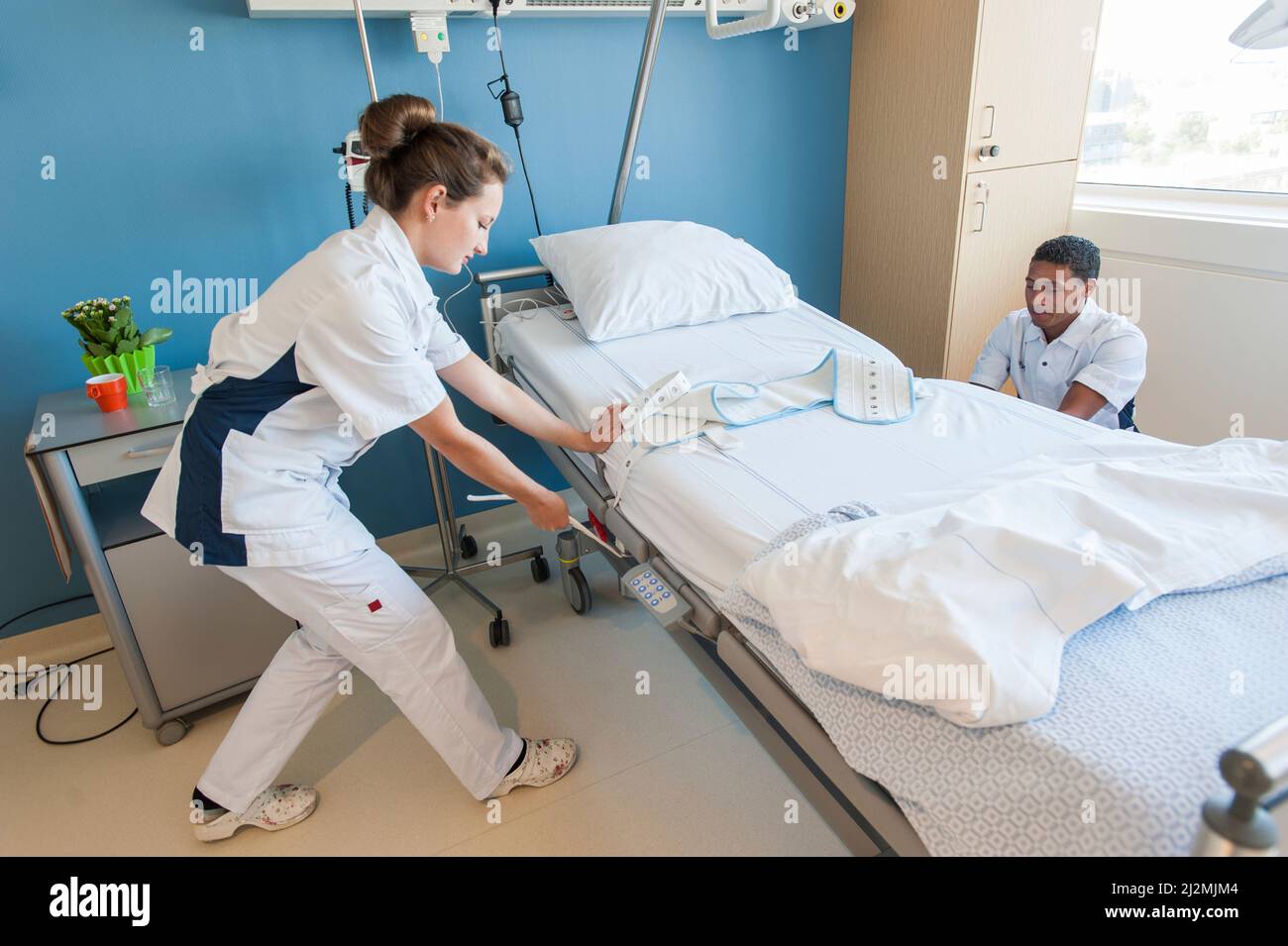Nurses attaching a restraint band to a patient's bed Stock Photo