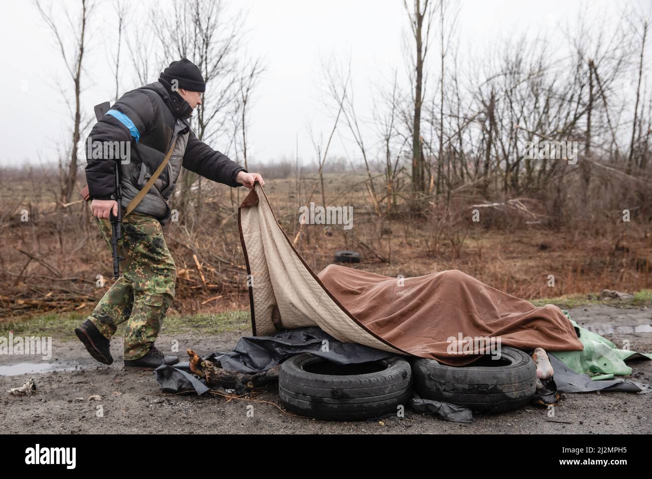 Bucha, Ukraine. 02nd Apr, 2022. (EDITORS NOTE: Image depicts death) A civilian defence force look at four dead civilians on the sidelines of the highway under a blanket at 20km from Kyiv. Almost 300 civilians have been killed along the road in between Zhytomyr and Kyiv near Bucha as most victims tried to cross the Buchanka river to reach the Ukrainian controlled territory and had been killed. Russia invaded Ukraine on 24 February 2022, triggering the largest military attack in Europe since World War II. Credit: SOPA Images Limited/Alamy Live News Stock Photo