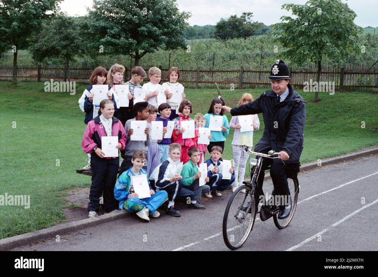 You put your right arm out... Pc David Wetton shows pupils at Lowerhouses C of E Junior, Infant and Nursery School how to make a right turn on their bicycles. Earlier the community policeman for Lowerhouses - who patrols his beat on a bike every day - presented cycling proficiency certificates, badges and bicycle locks to 19 pupils who had passed the proficiency test. 26th June 1991. Stock Photo