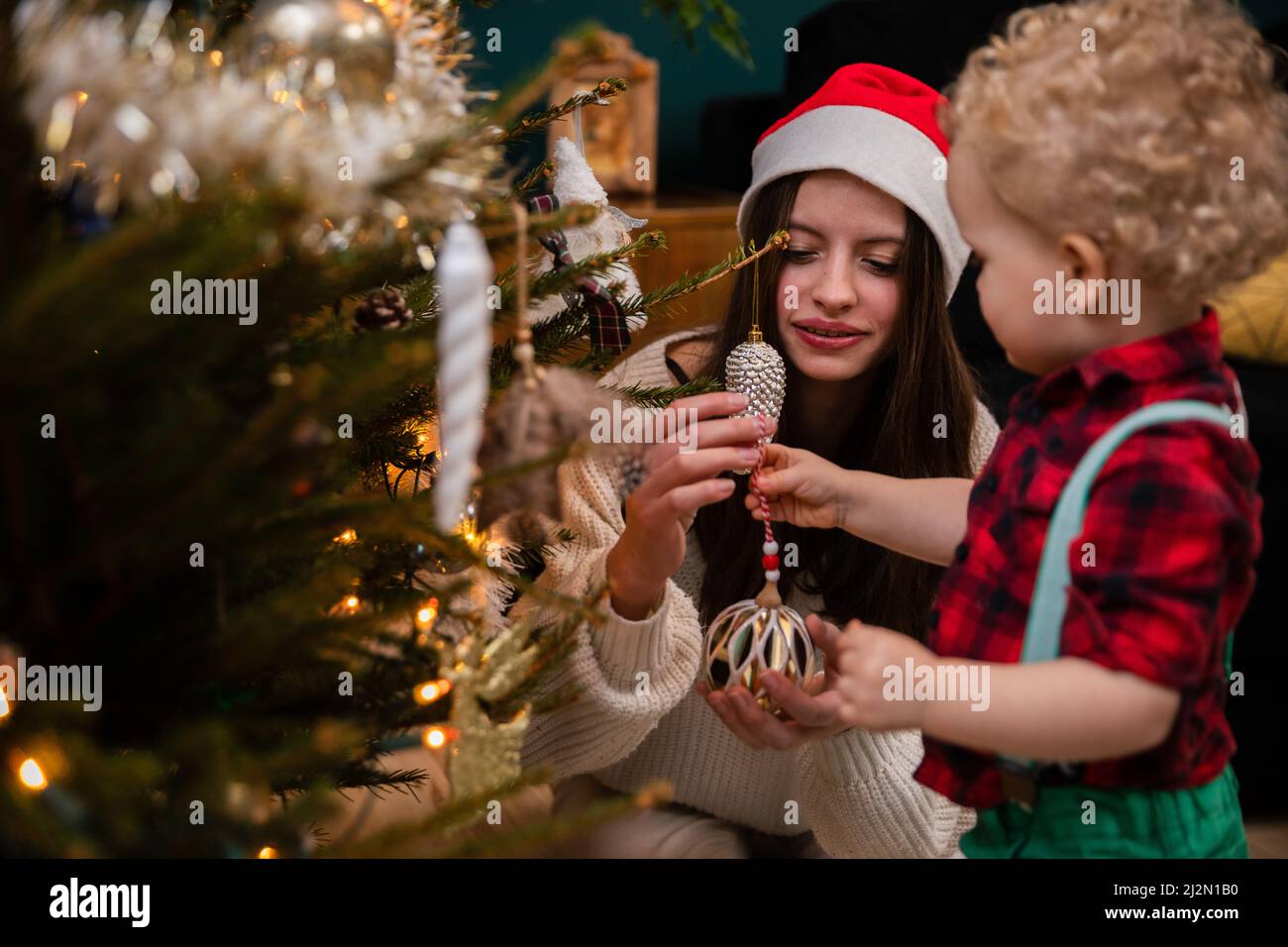 A sister helps her young brother hang ornaments for the Christmas tree. Stock Photo