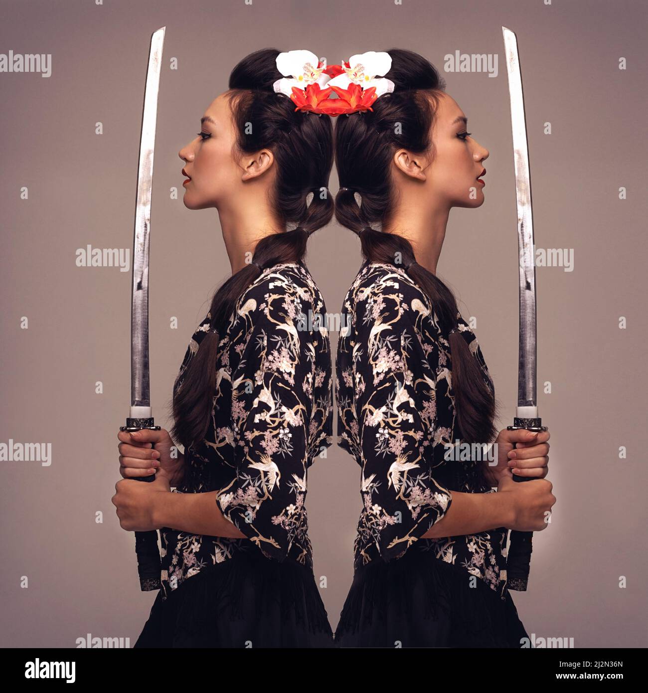 Shes a warrior. Mirrored studio shot of an attractive young woman holding a samurai sword. Stock Photo