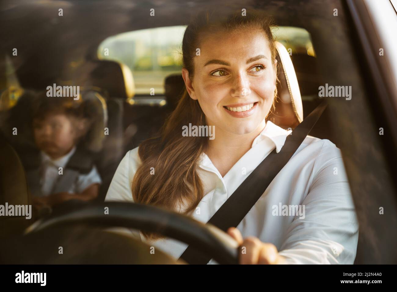 Young white woman driving car while her son sitting in baby seat on
