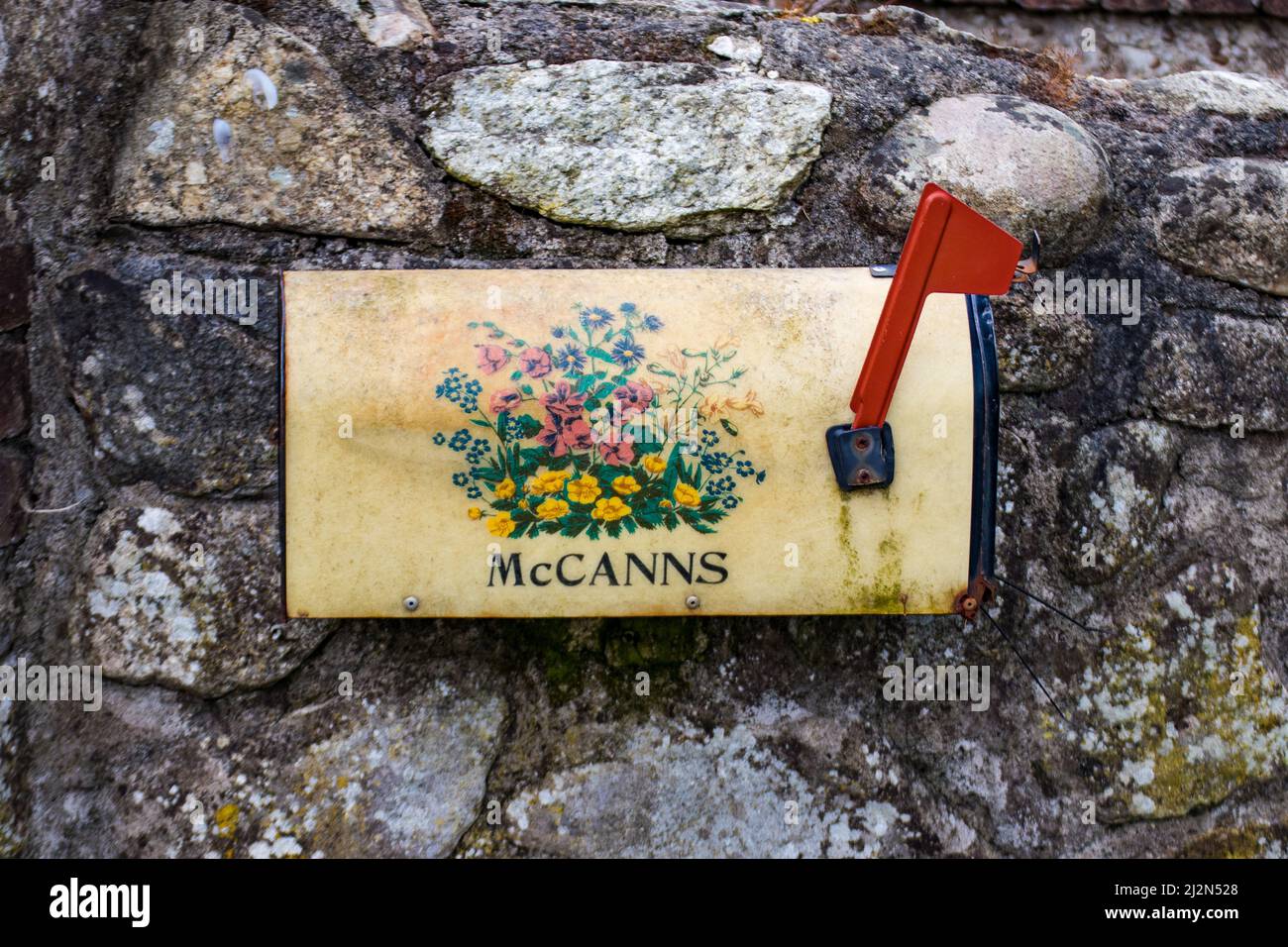 Old weathered metal mailbox mounted on gray stone wall with red flag