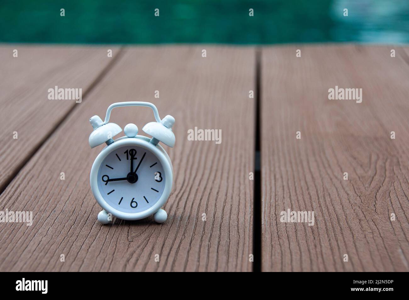 White alarm clock on wooden floor with blurred swimming pool background