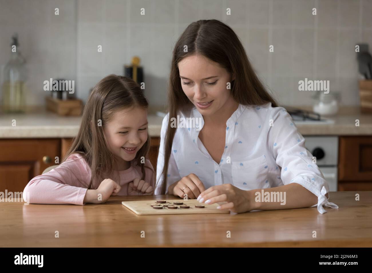 Happy mom and daughter girl engaged in learning board game Stock Photo