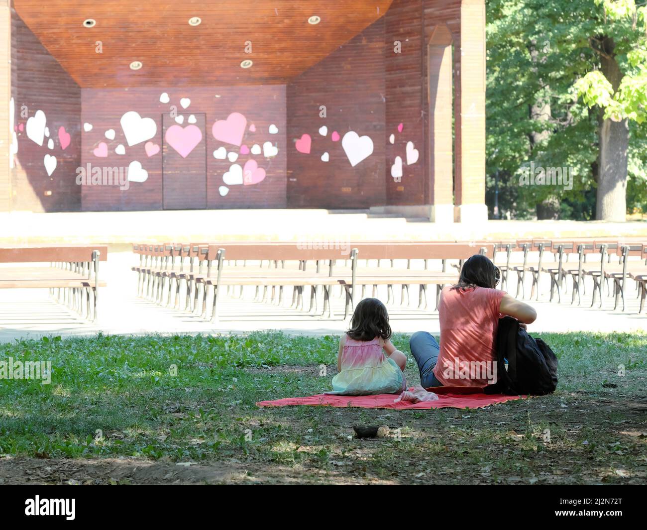 woman and child sitting in a sofia park in front of theater scene decorated with shape of heart Stock Photo