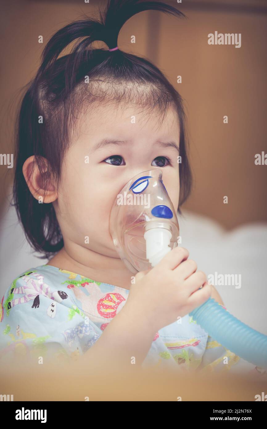 Cute asian child holds a mask vapor inhaler for treatment of asthma on ...