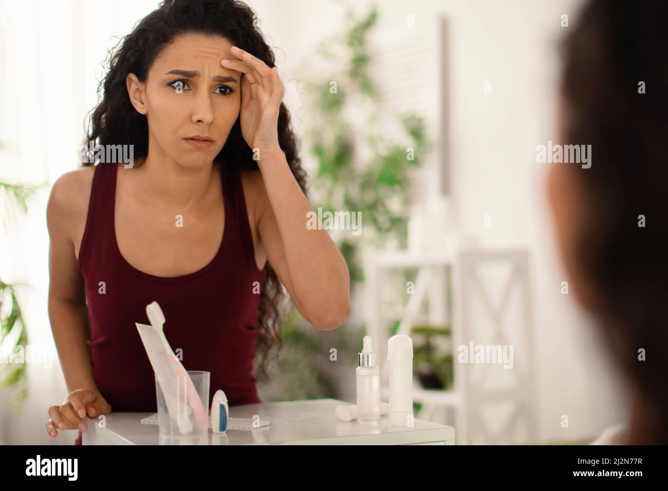 Unhappy millennial woman looking at her reflection in mirror, checking ...