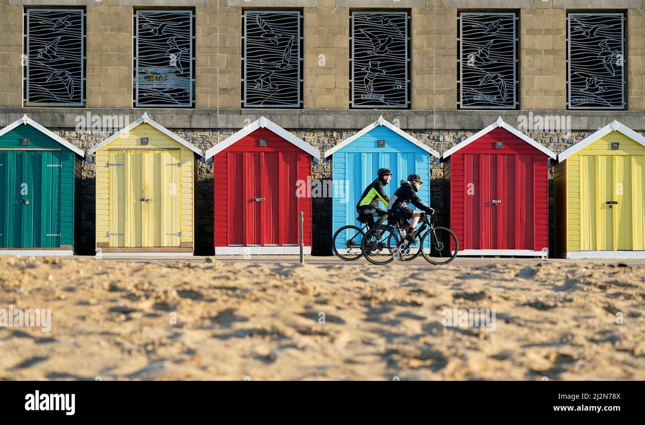 People cycle past beach huts on Boscombe beach in Dorset. Picture date: Sunday April 3, 2022. Stock Photo