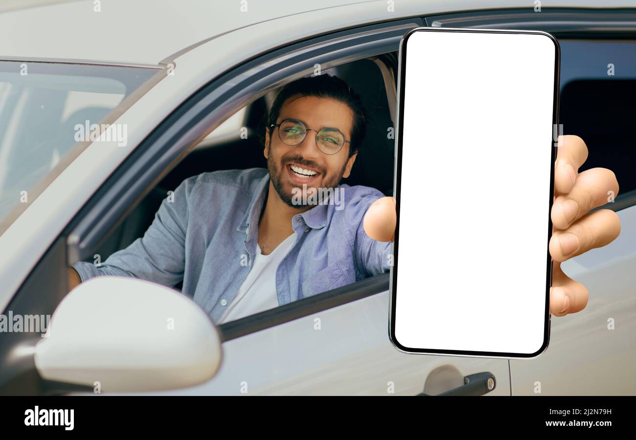 Happy Young Indian Man Showing Big Blank Smartphone While Sitting In Car Stock Photo