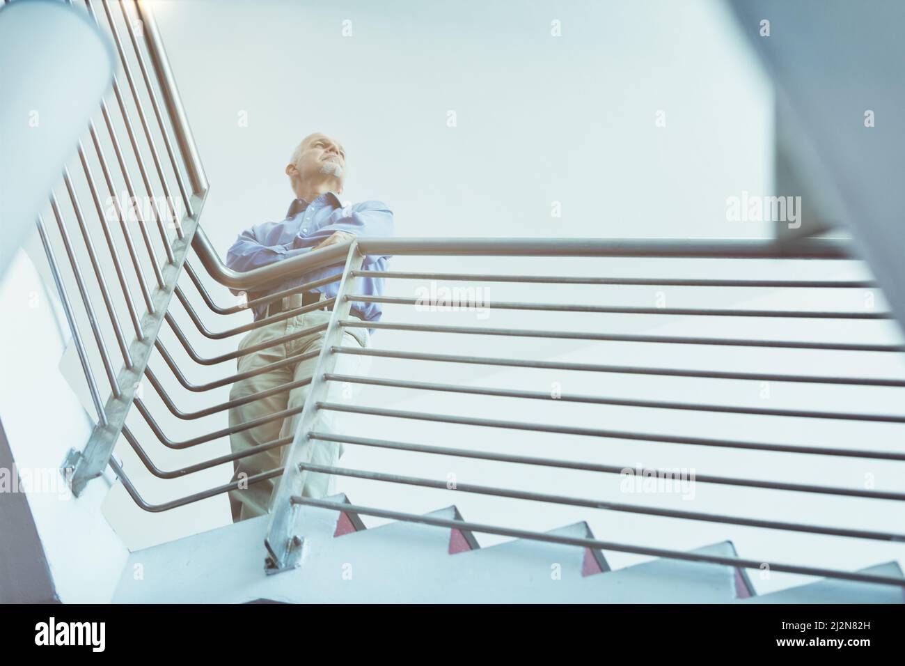 View from the bottom of a man no longer young at the top, in a corporate environment, a modern staircase with clean lines, looks towards the horizon b Stock Photo