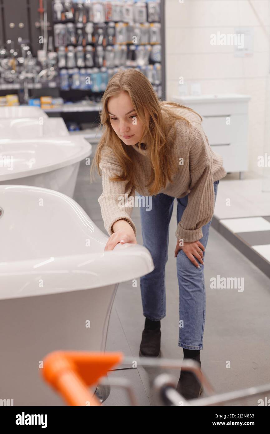 Woman choosing new acrylic bathtub in hardware store. Home bathroom