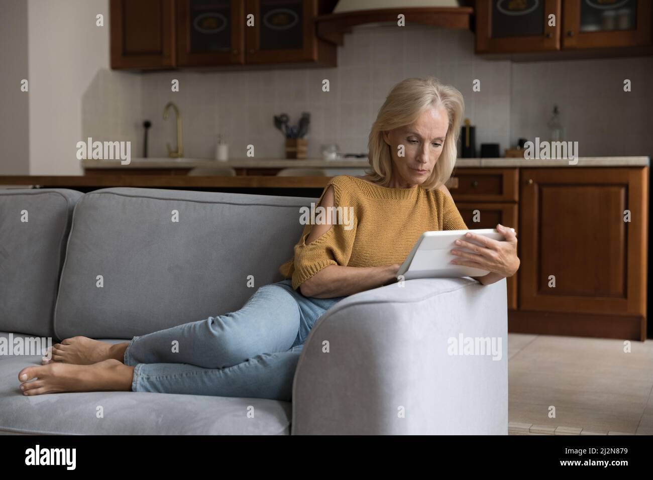 Focused middle aged customer lady using tablet computer at home Stock Photo