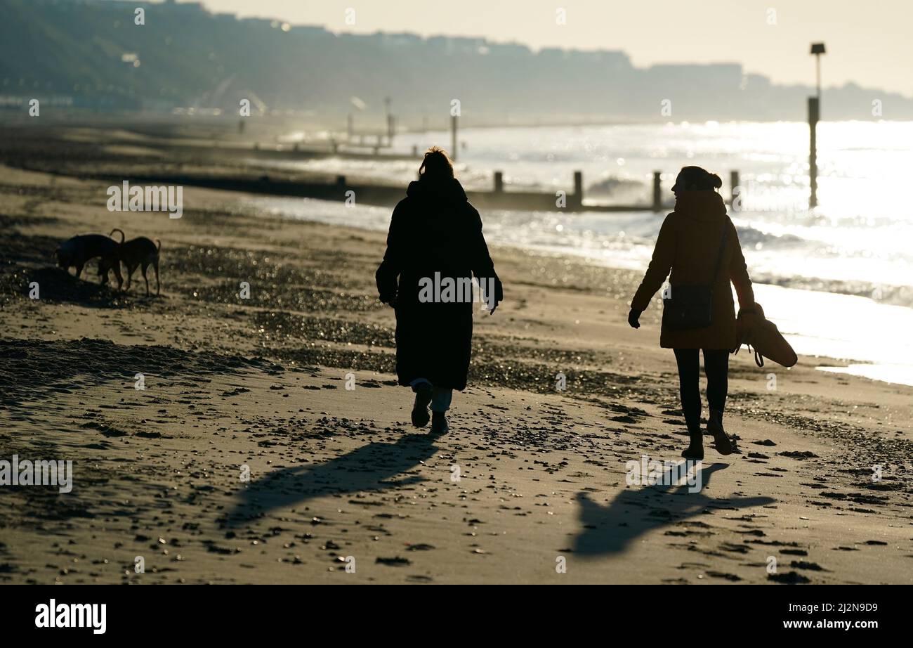 People walk along the beach as the sun rises over Boscombe beach in Dorset. Picture date: Sunday April 3, 2022. Stock Photo