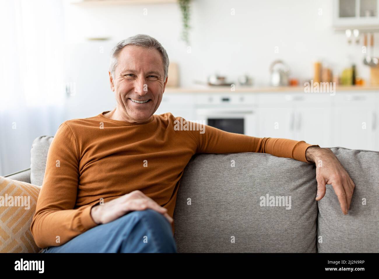 Smiling mature man sitting on the couch and posing Stock Photo - Alamy