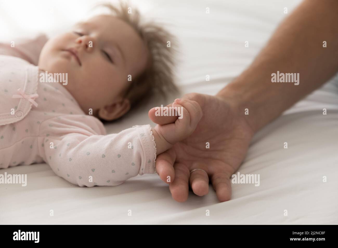 Serene adorable sleepy baby catching dads thumb, holding finger Stock Photo