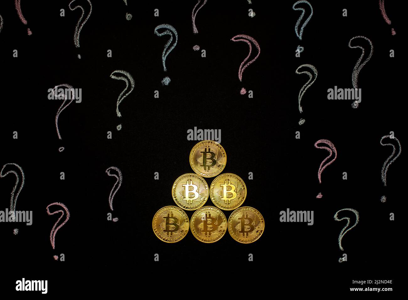 Hand holding Bitcoin virtual money against blackboard with question marks. Digital currency concept Stock Photo