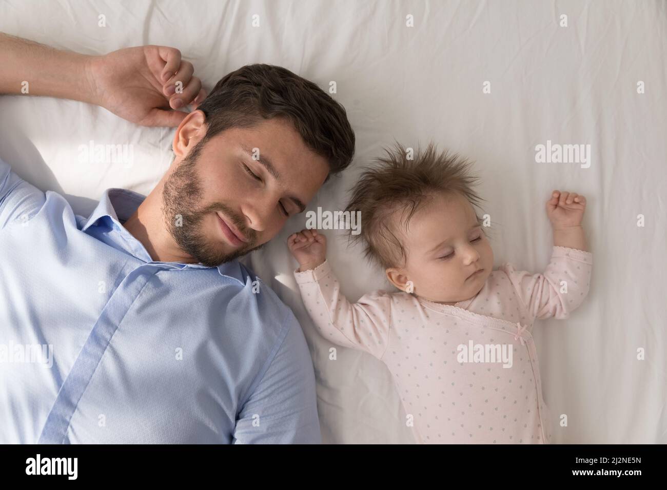 Happy peaceful dad and cute baby daughter sleeping in bed Stock Photo