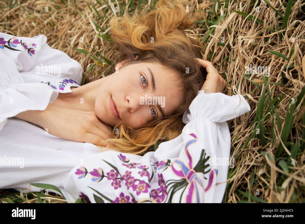beautiful girl 17-19 years old in an embroidered Ukrainian traditional shirt lies in dry grass. View from above. I am Ukrainian. Stand with Ukraine Stock Photo