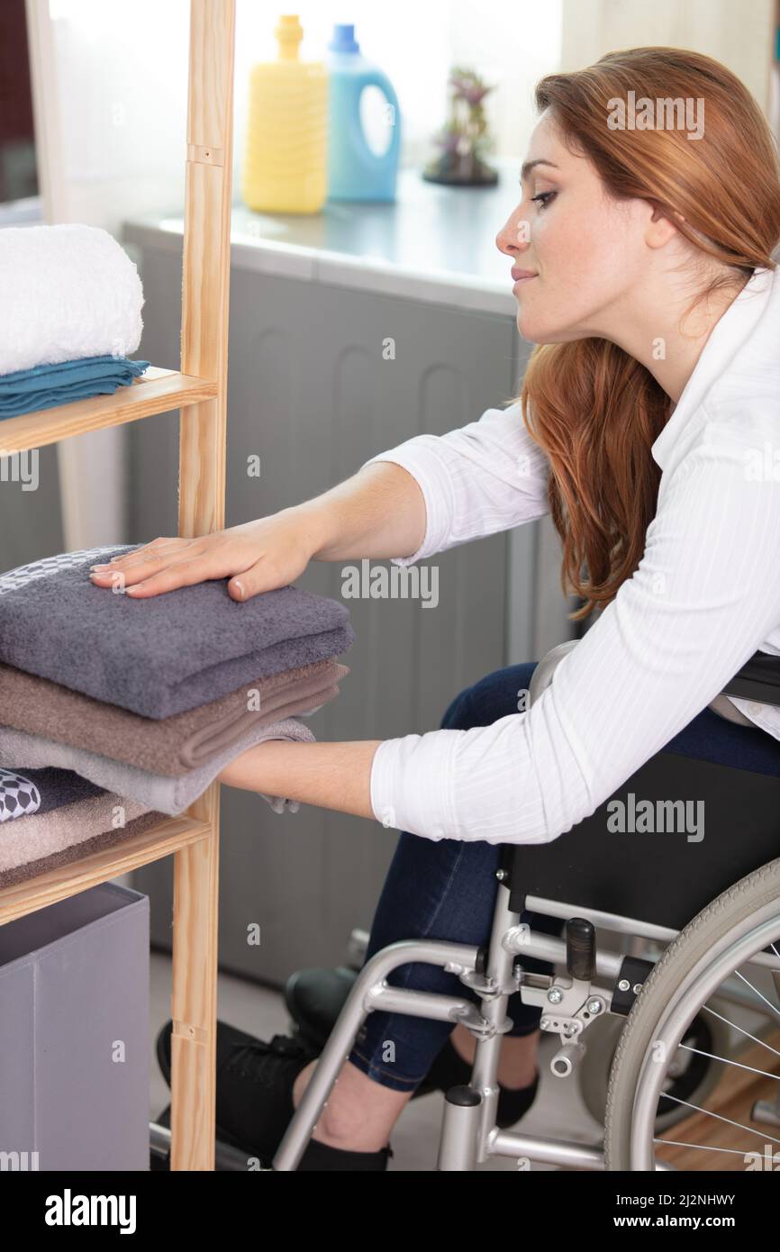 young disabled woman in wheelchair putting away clean laundry Stock Photo